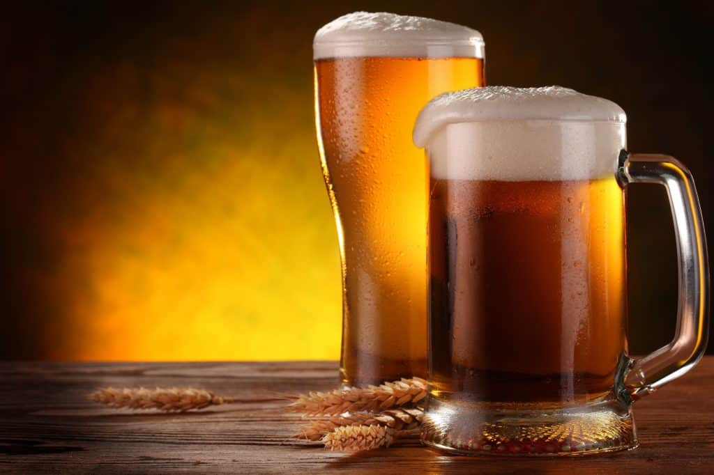 a mug of beer with a tall glass of beer lit up from behind on a wooden table, grab a drink at one of the breweries in quad cities