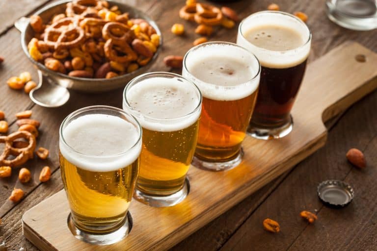 a flight of four beers sits on a table with snack food like pretzels