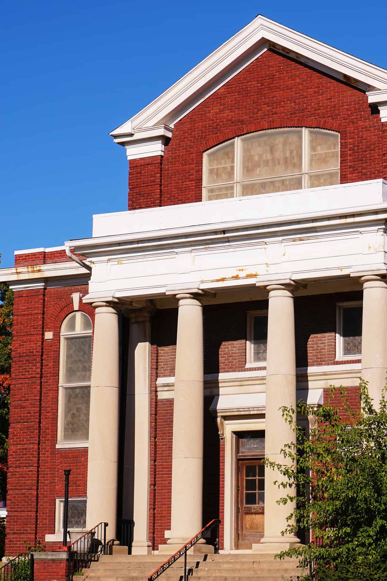 an old brick building stands tall with huge pillars out front under a blue sky