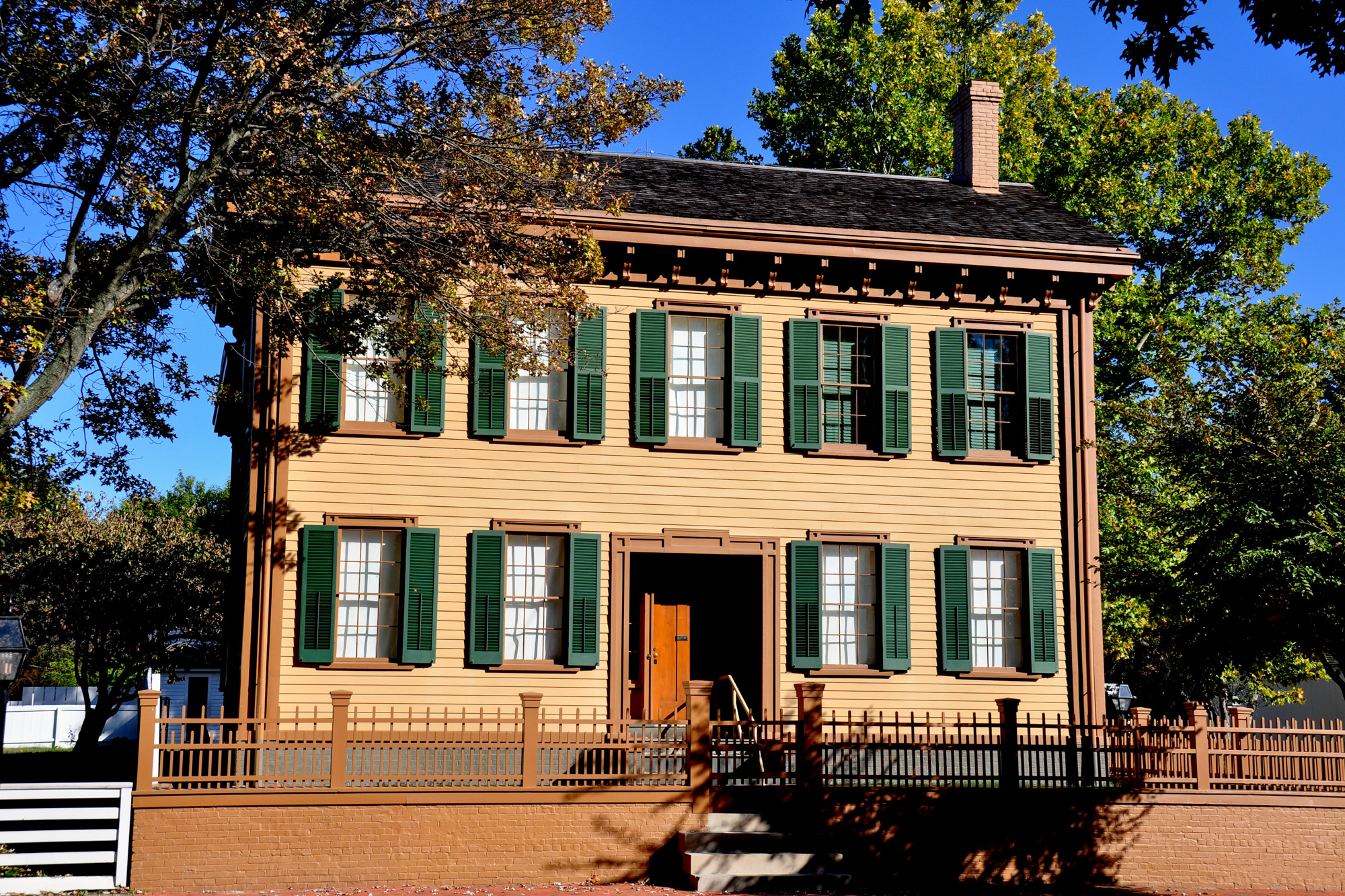 abraham lincolns home with yellow siding and green window shades around each window