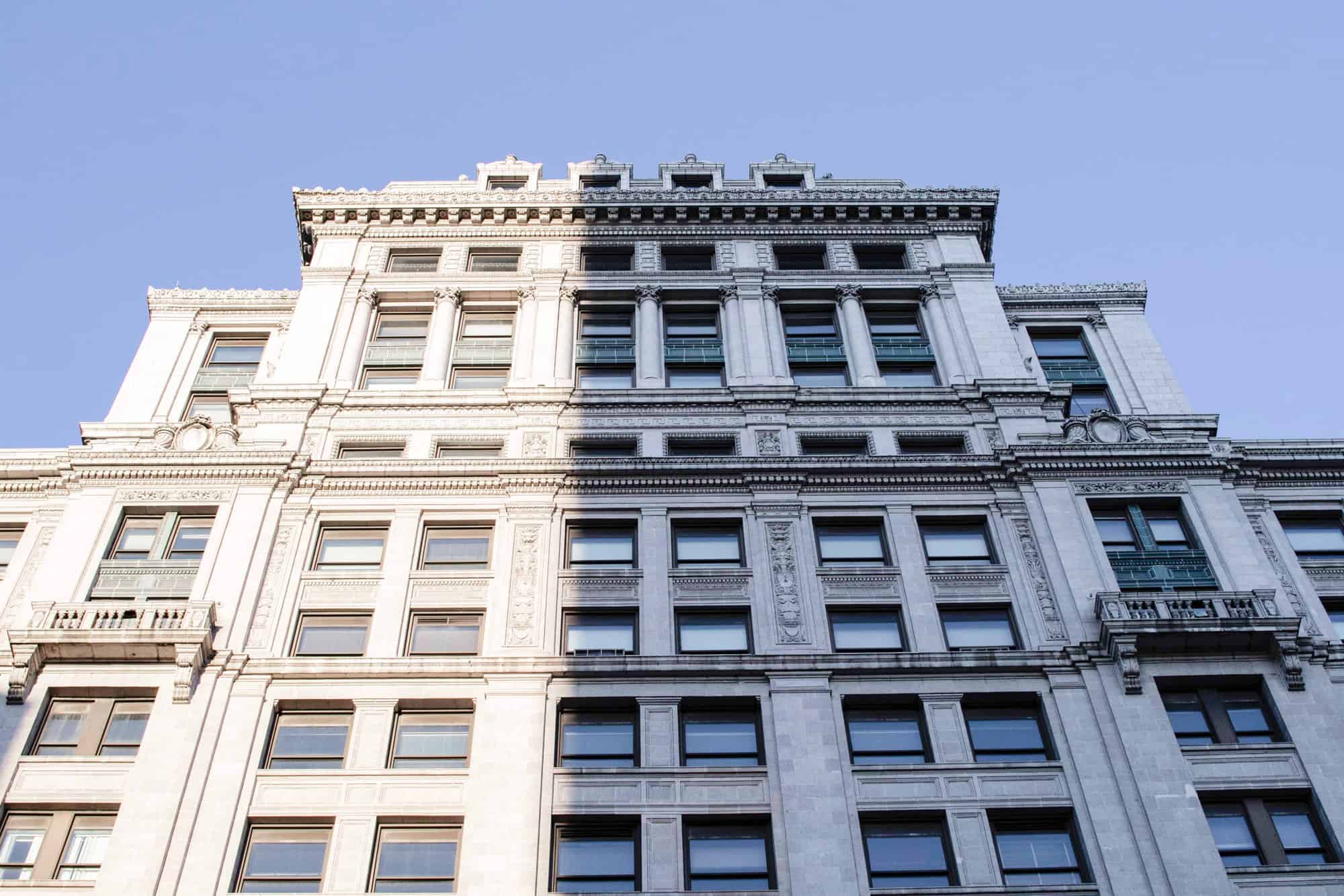 a white building downtown looking up at it from a bugs view, full of windows and in partial sunlight partial shadow